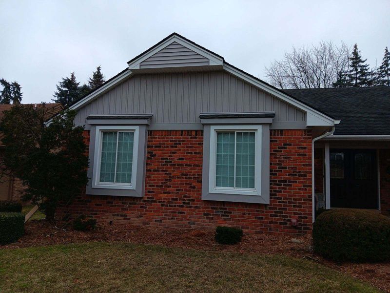 Red brick house with two windows, gray siding, and a dark roof.