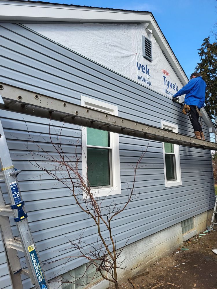 Person installing blue siding on a house, using a ladder.