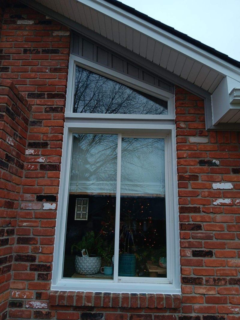 Brick building with white-framed window. A slanted triangular window sits above a double-pane window.