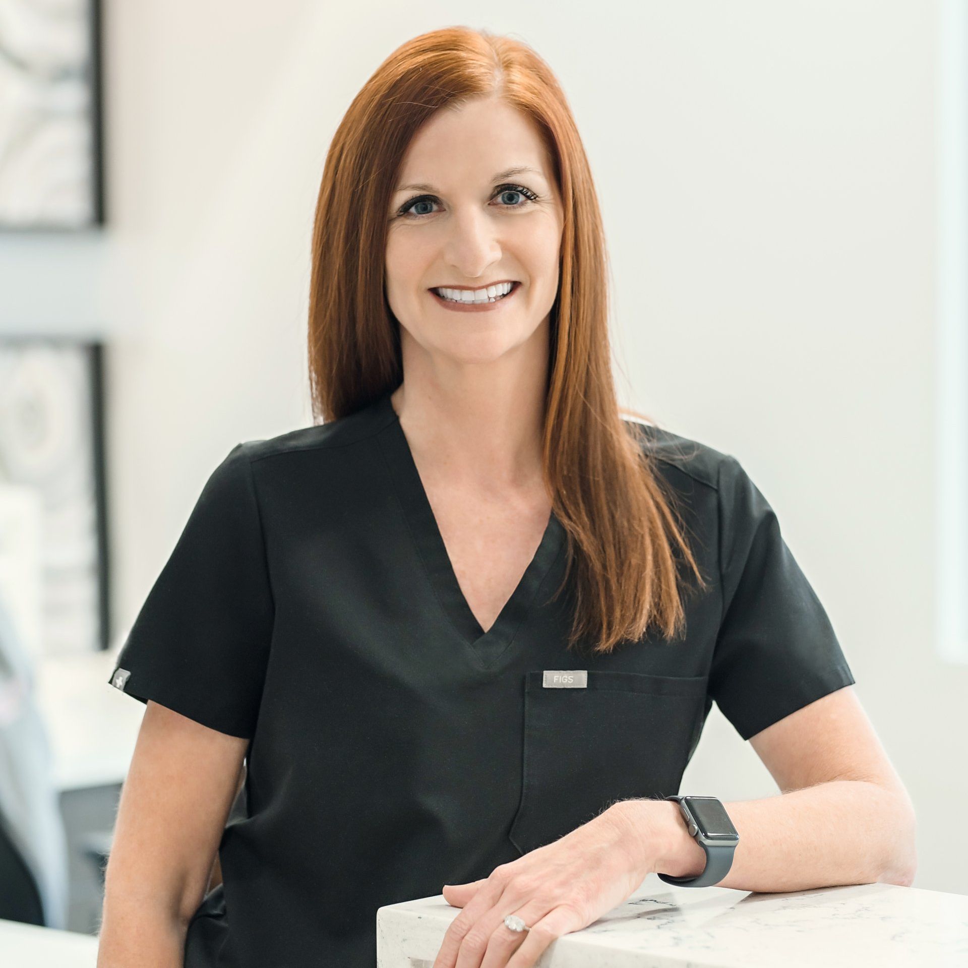 A woman in a black scrub top is sitting at a counter and smiling.