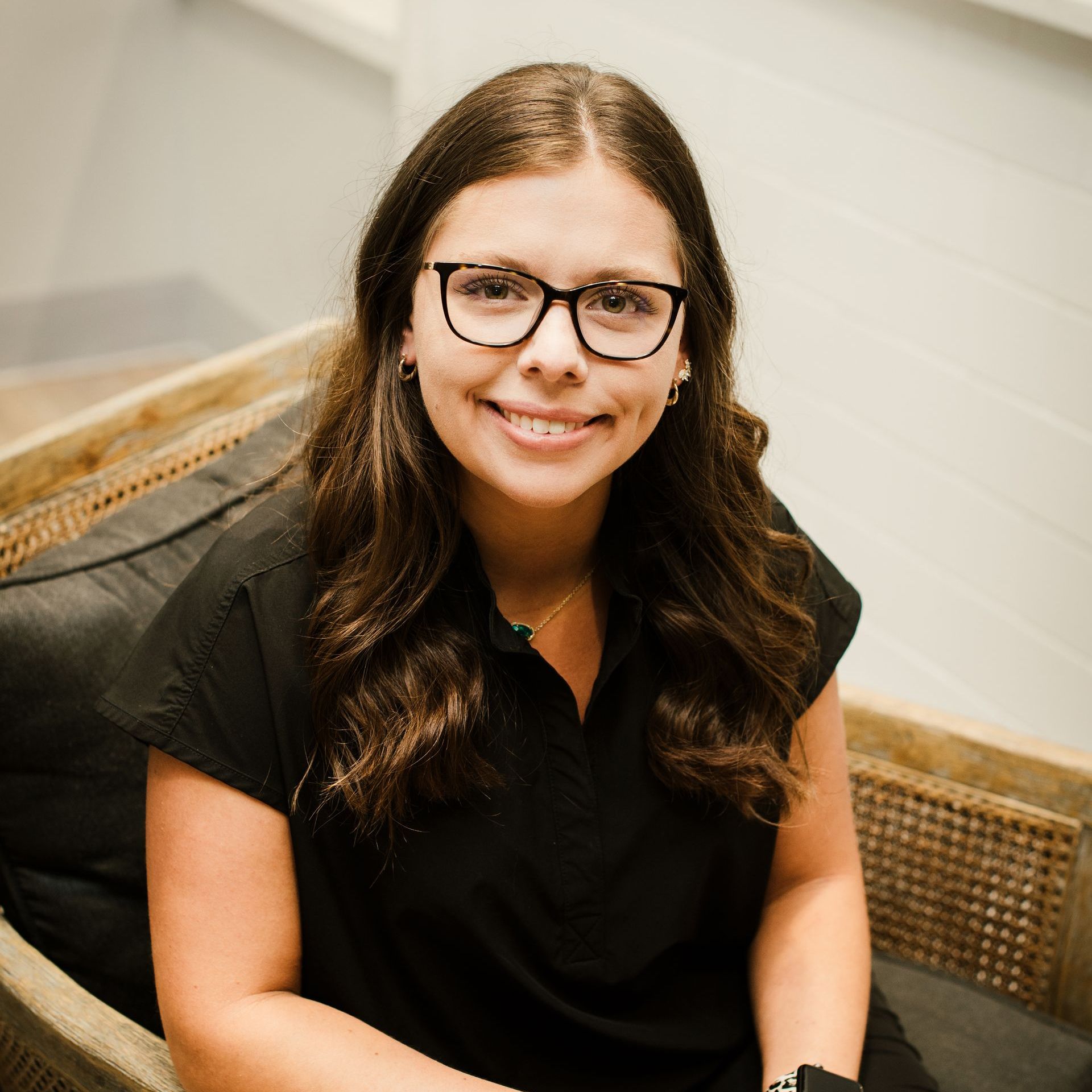 A woman wearing glasses and a black shirt is sitting in a chair.