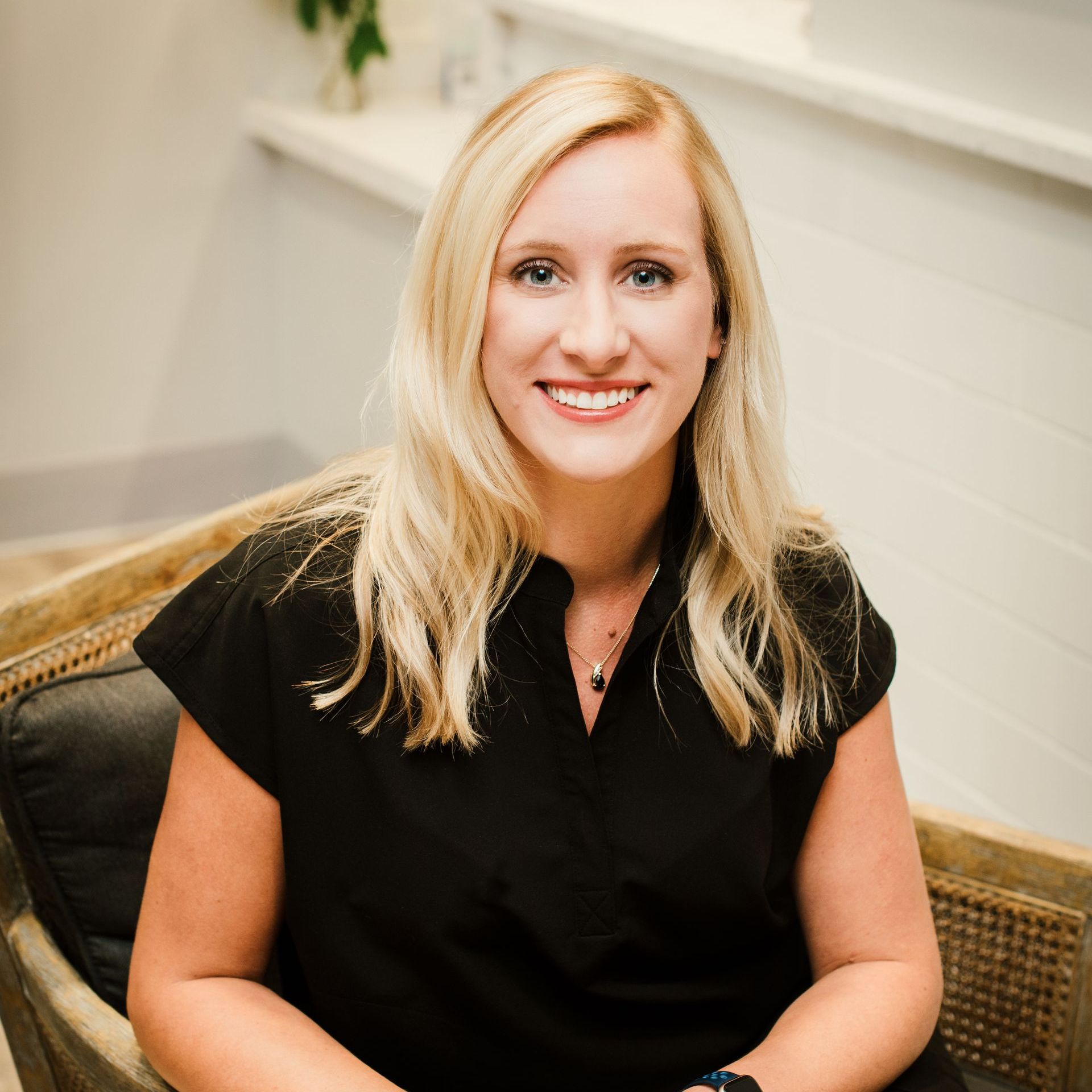 A woman in a black shirt is sitting in a chair and smiling for the camera.