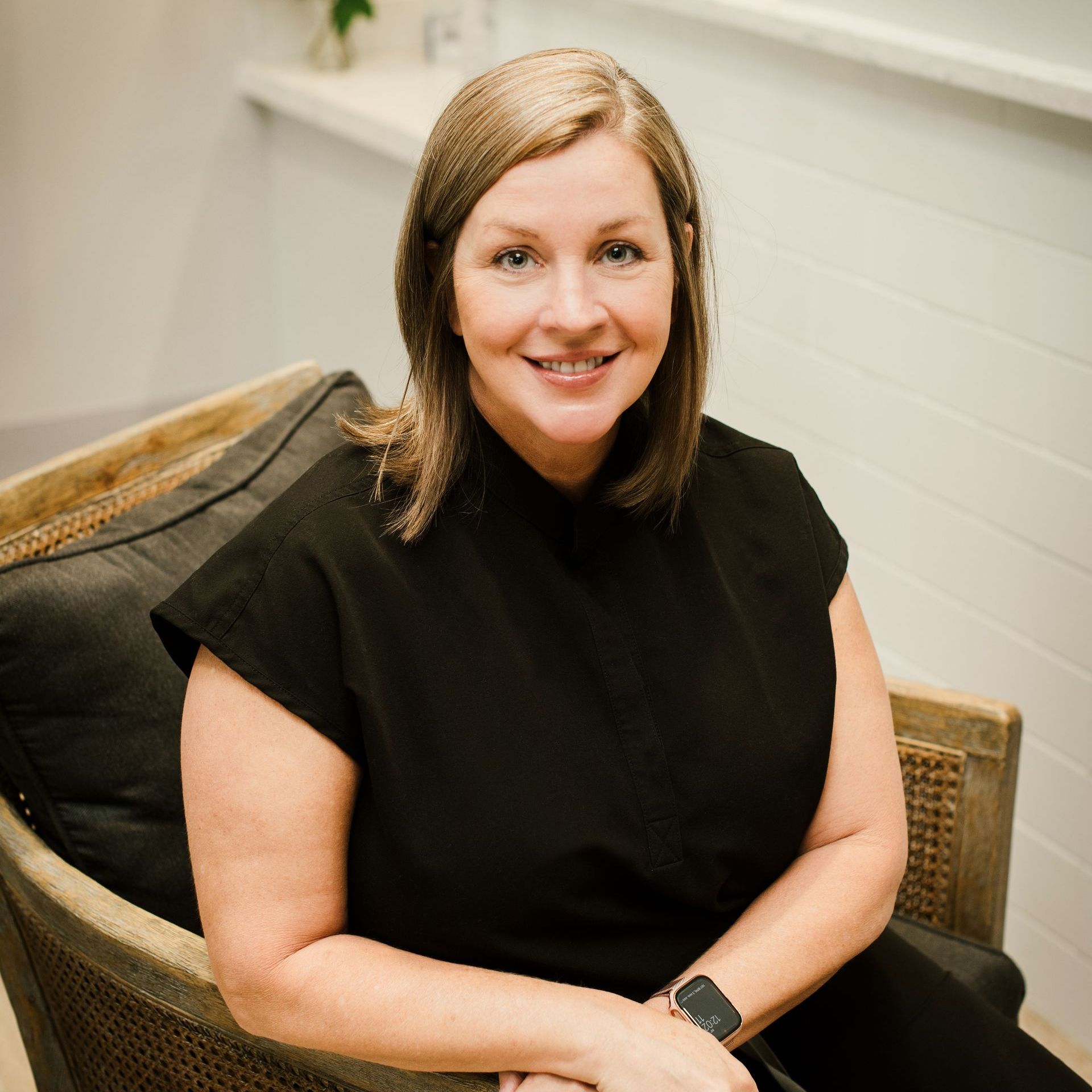 A woman in a black shirt is sitting in a chair and smiling.