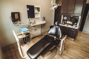 A dental office with a black dental chair and cabinets.