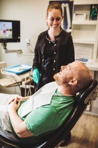 A man is sitting in a dental chair while a woman stands behind him.