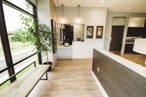 A waiting room with a bench and a plant in front of a window.