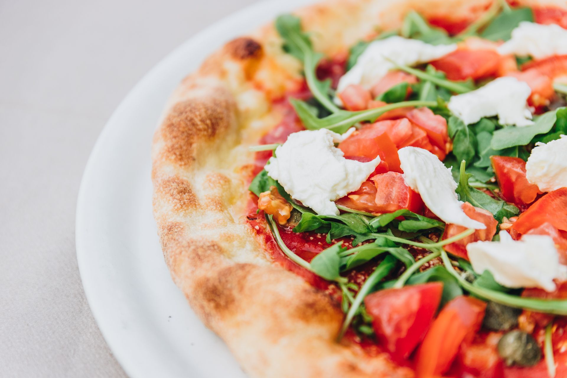 Una pizza fresca condita con salsa di pomodoro, rucola, pezzi di formaggio bianco e pomodori a cubetti