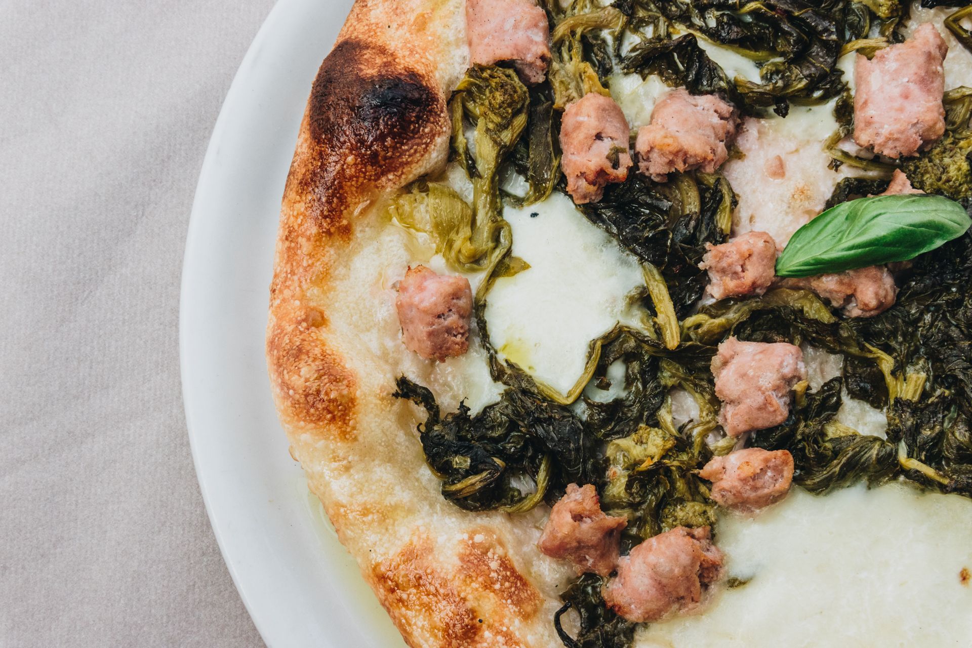 Una pizza condita con salsiccia, verdure amare e formaggio fuso su un piatto, ripresa dall'alto.