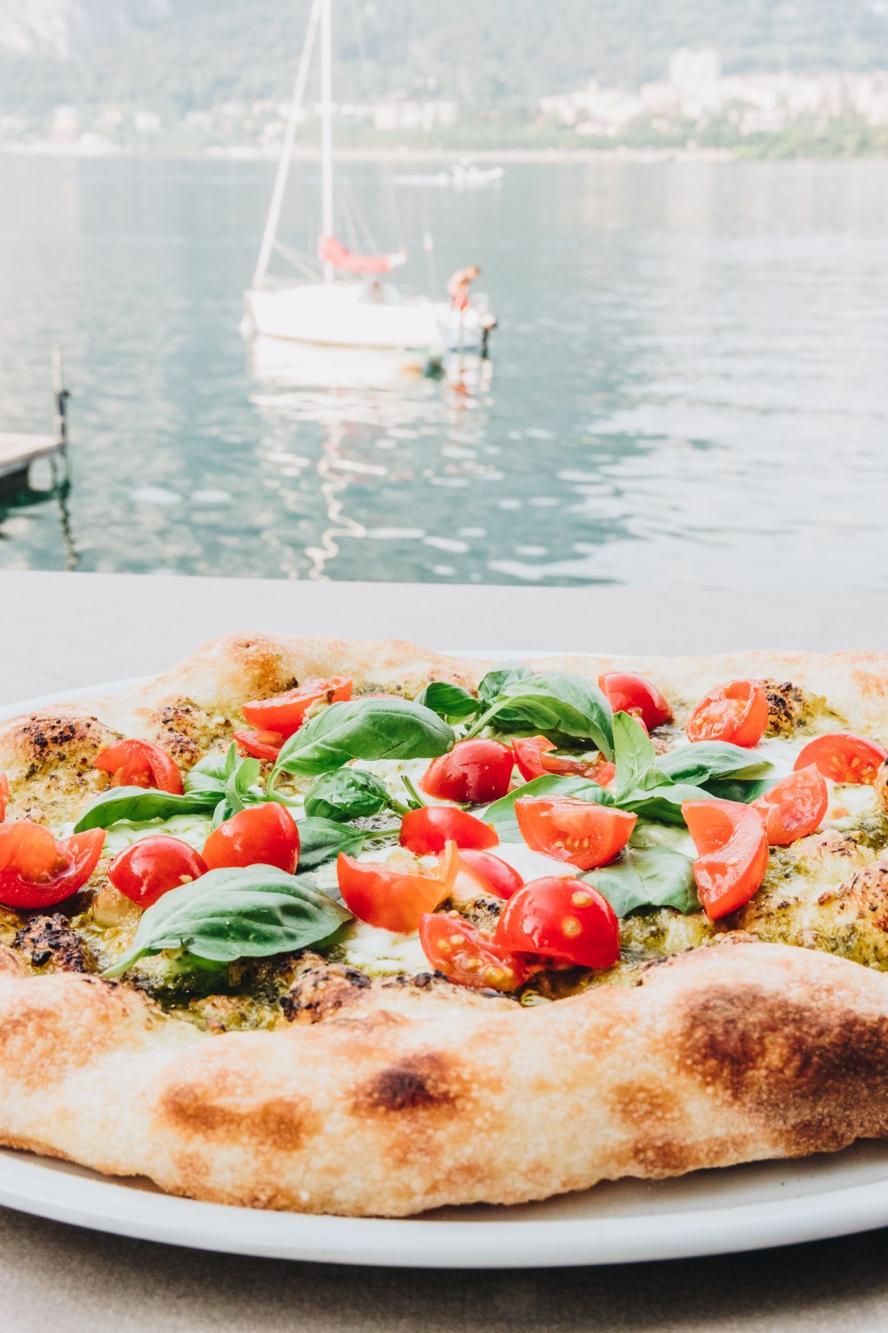 Una pizza condita con pomodorini e basilico fresco, servita su un piatto con vista su lago