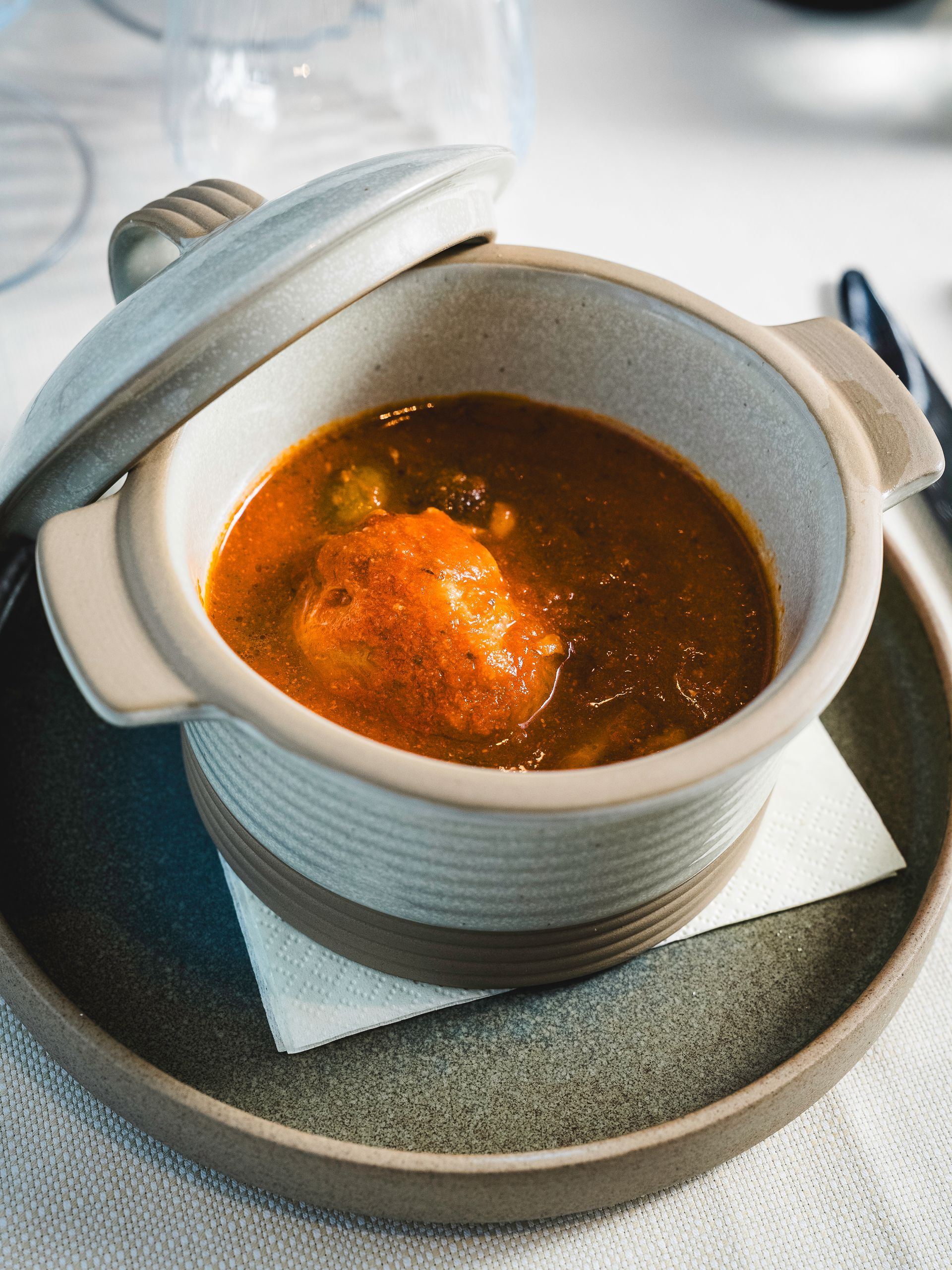 Zuppa in una ciotola di ceramica con coperchio su un piatto, su un tavolo.