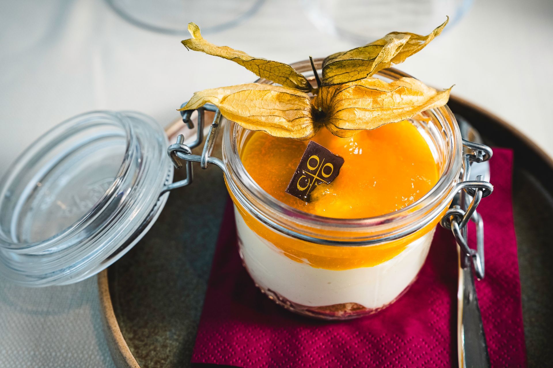 Dessert in barattolo con guarnizione di mango giallo e cioccolato; su un piatto con tovagliolo rosso.