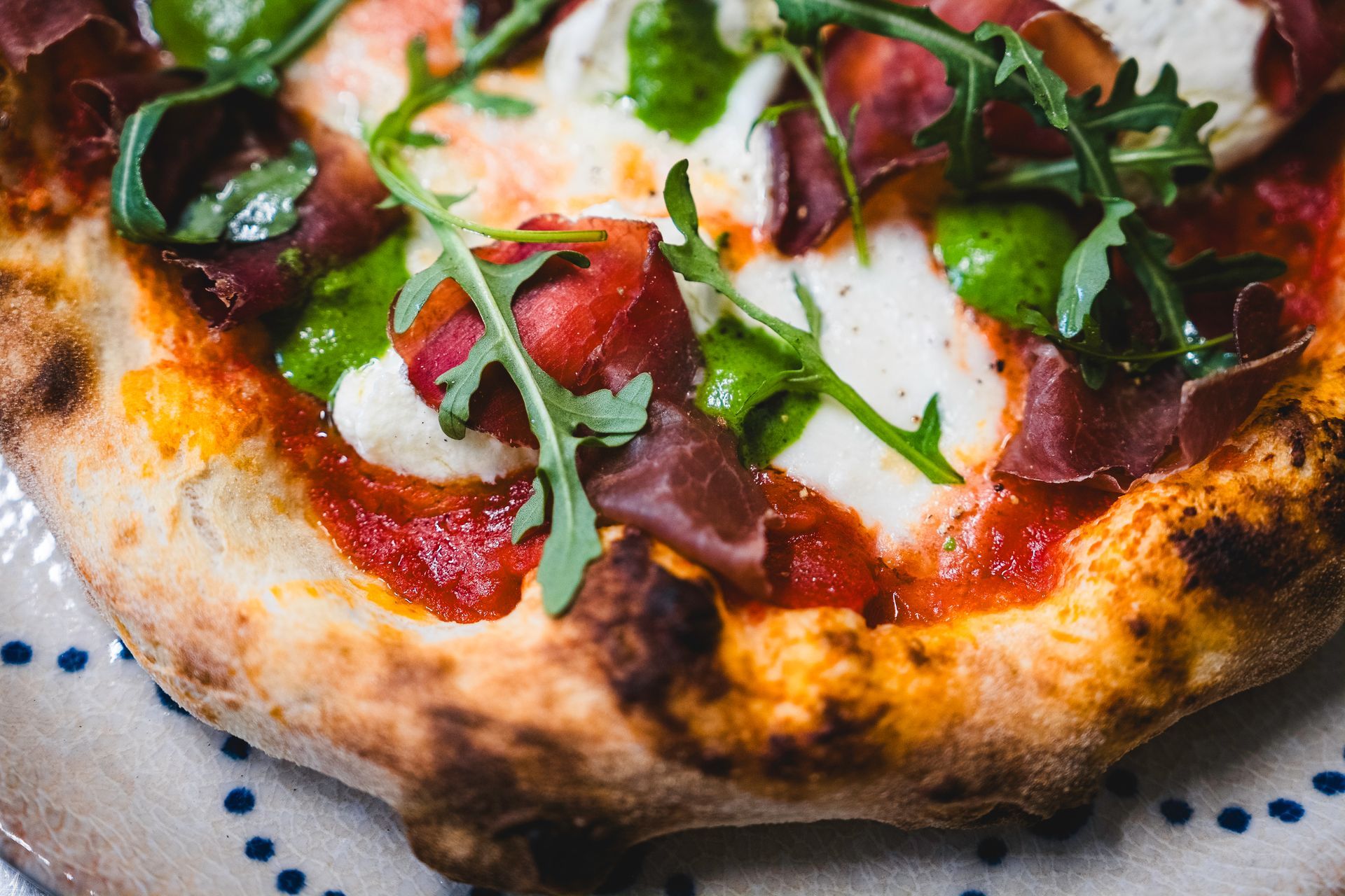Pizza con prosciutto, rucola, mozzarella e pesto su una base rustica.