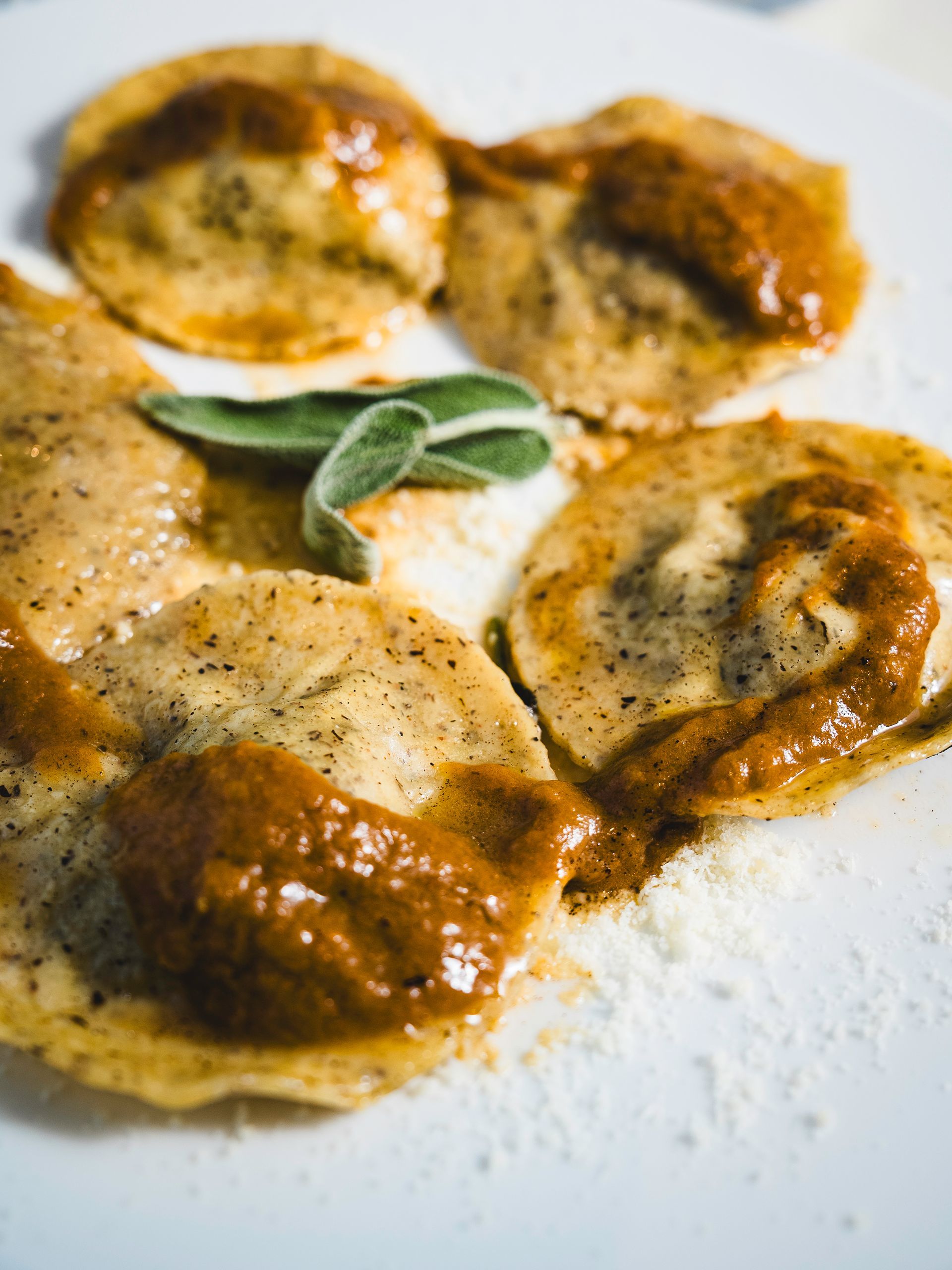 Ravioli rotondi con salsa all'arancia e una foglia di salvia su un piatto bianco.