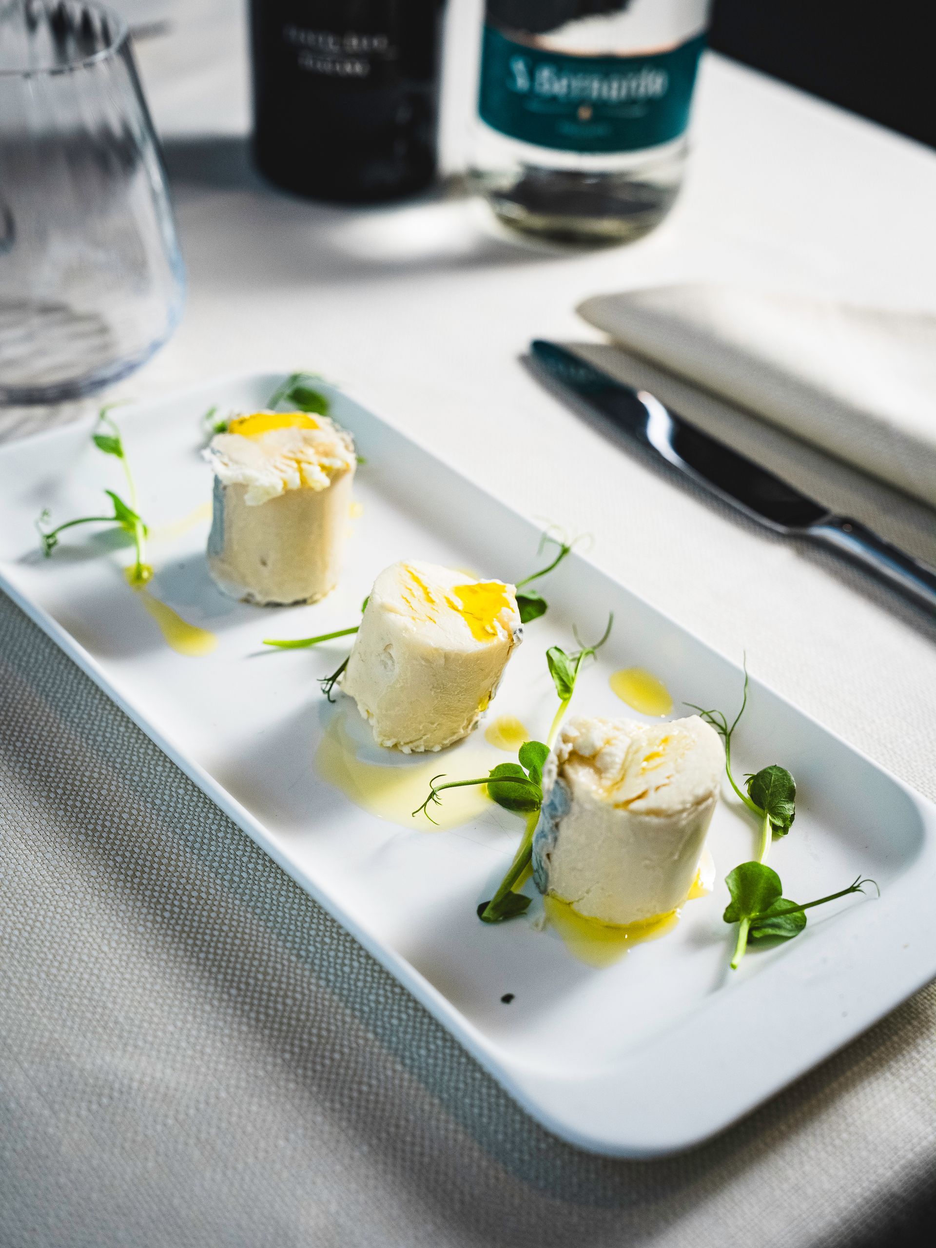 Tre antipasti cilindrici su un piatto rettangolare bianco.