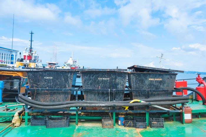 Black containers on a boat deck with other boats in the background under a blue sky.