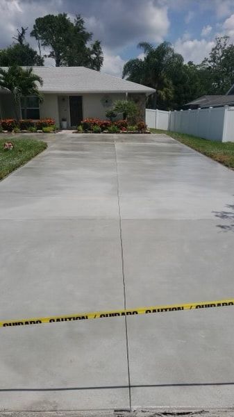 Newly poured concrete driveway with caution tape in front of a light-colored house.