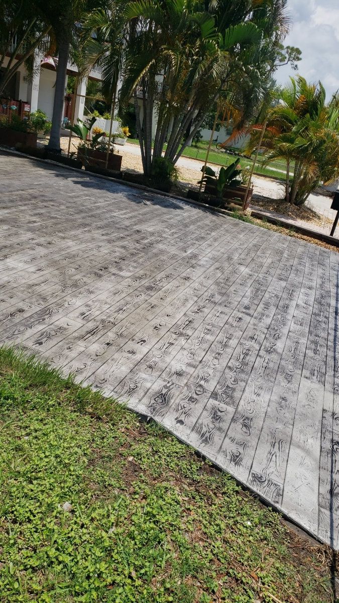 Gray brick driveway with green grass and trees.