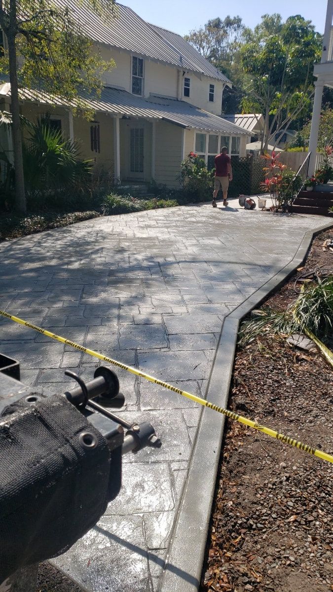 Stamped concrete driveway in front of a house. A person walks near the end. Yellow caution tape.