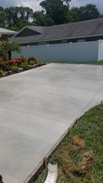Newly poured concrete driveway with a white fence and trimmed lawn.