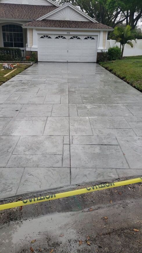 Stamped concrete driveway in front of a white garage door, with caution tape across the bottom.