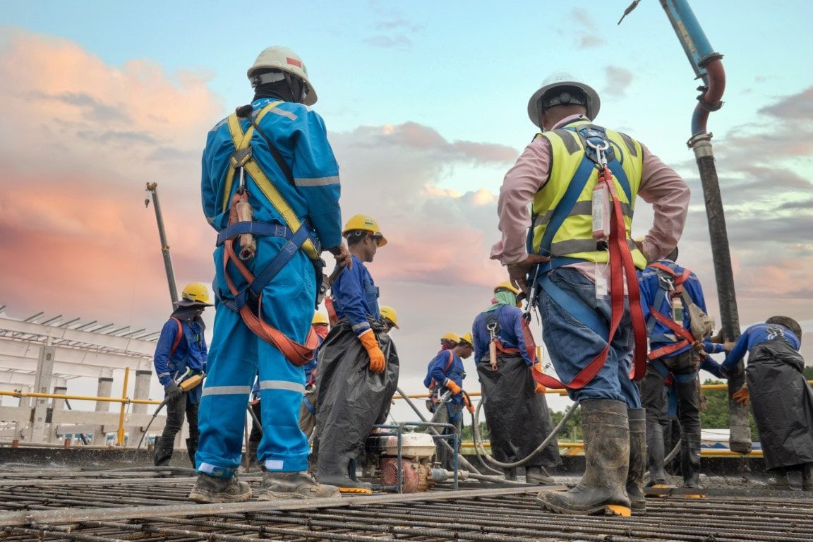 Construction workers in blue and yellow protective gear on a construction site; sky in background.
