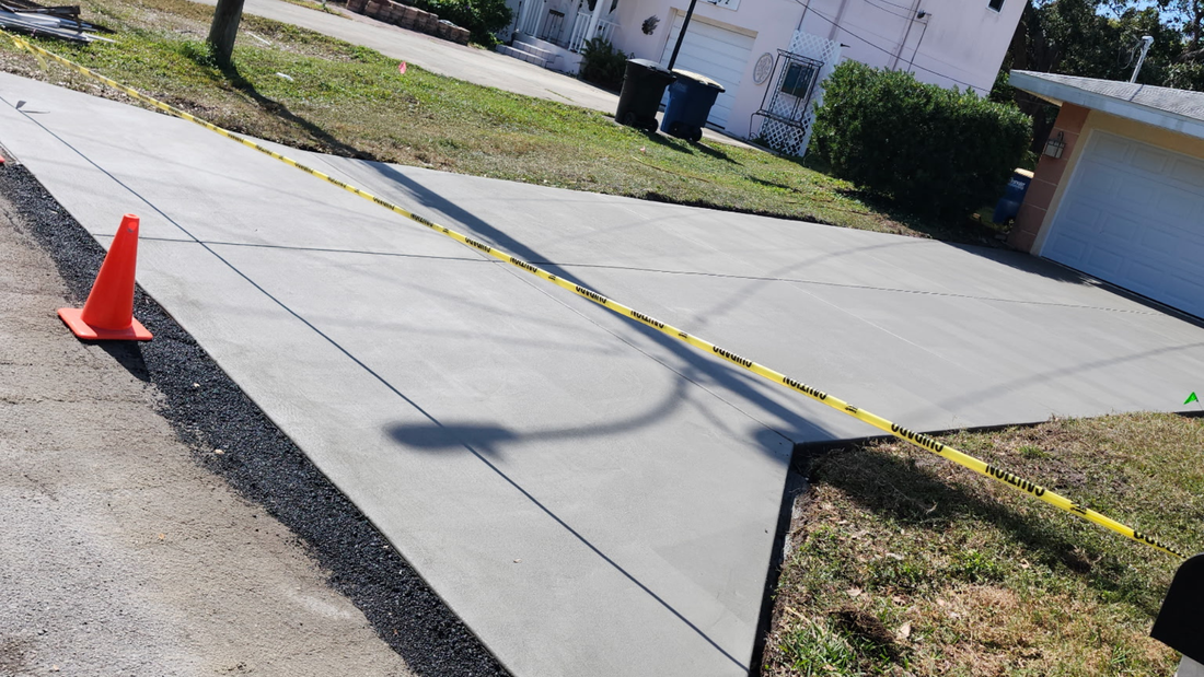 Newly paved concrete driveway with orange cone and caution tape.