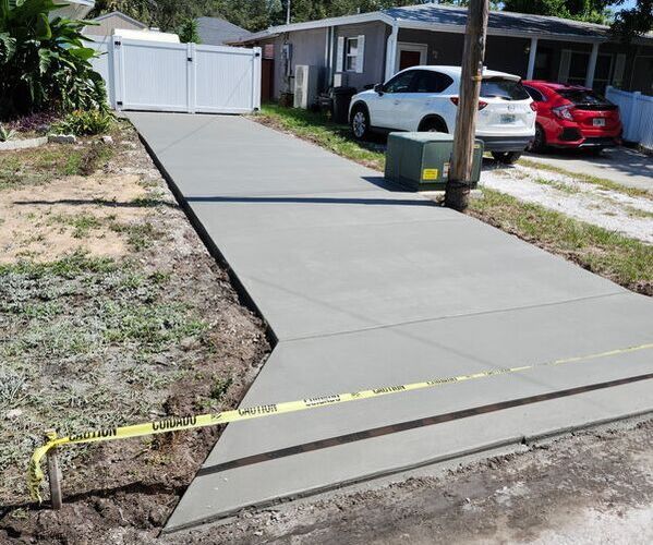 Newly poured concrete driveway with a white gate and cars parked in front of a house.