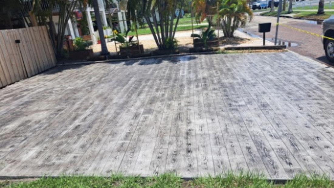 Wooden deck, weathered and gray, in front of a yard with plants and a fence.