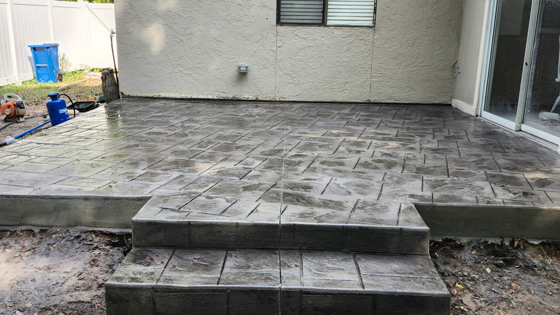Concrete patio with stamped brick pattern and steps leading up to a sliding glass door.