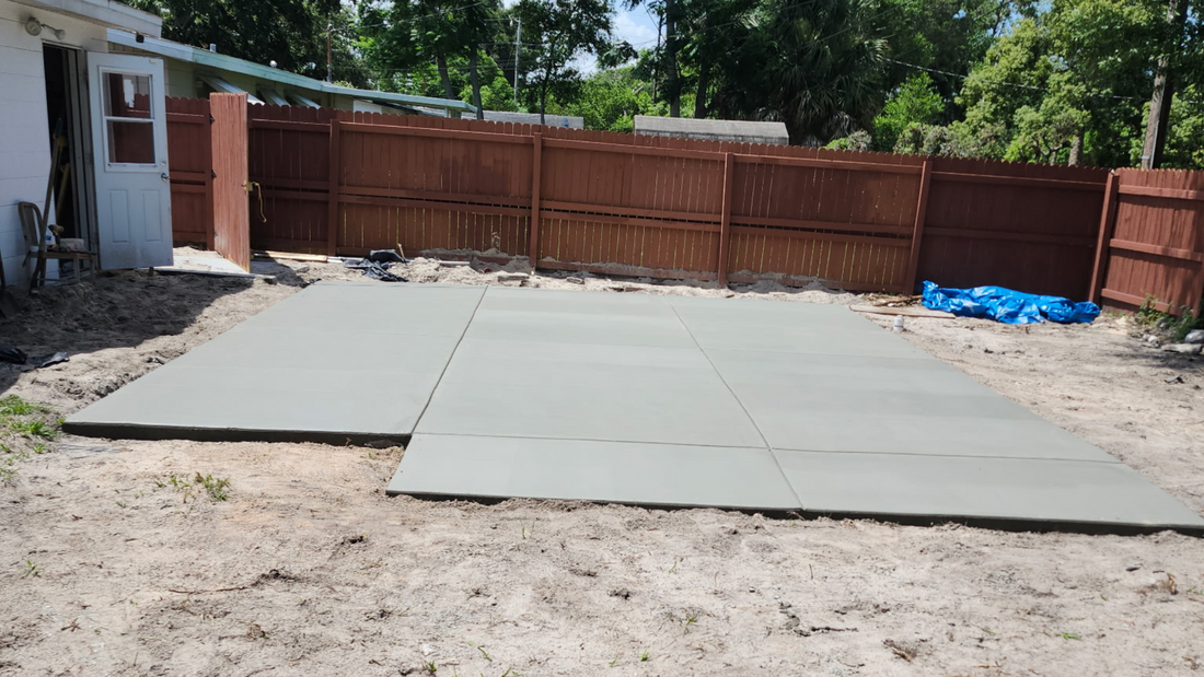 Newly poured concrete patio in a backyard with a wooden fence.