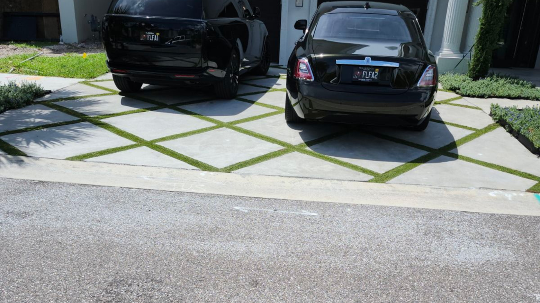 Two black cars parked on a driveway with a concrete grid filled with green grass.