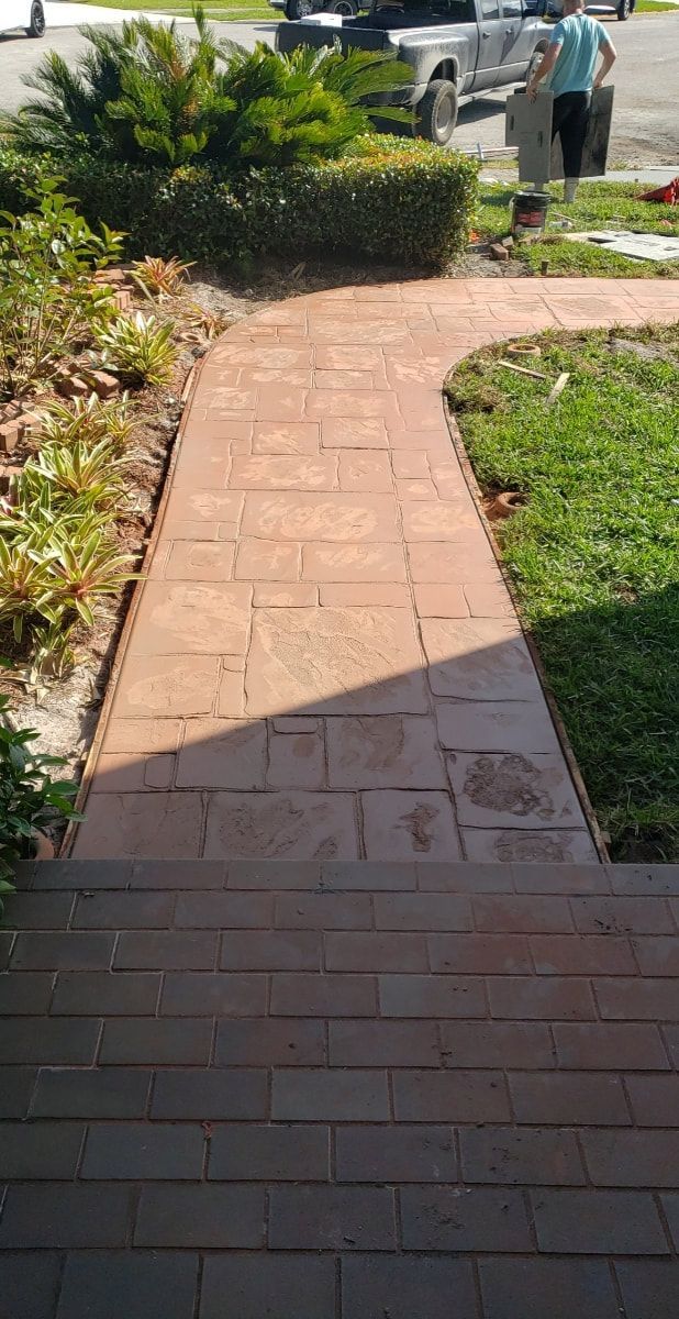 Brick pathway leading to a building's entrance. Green grass and shrubs border the walkway.