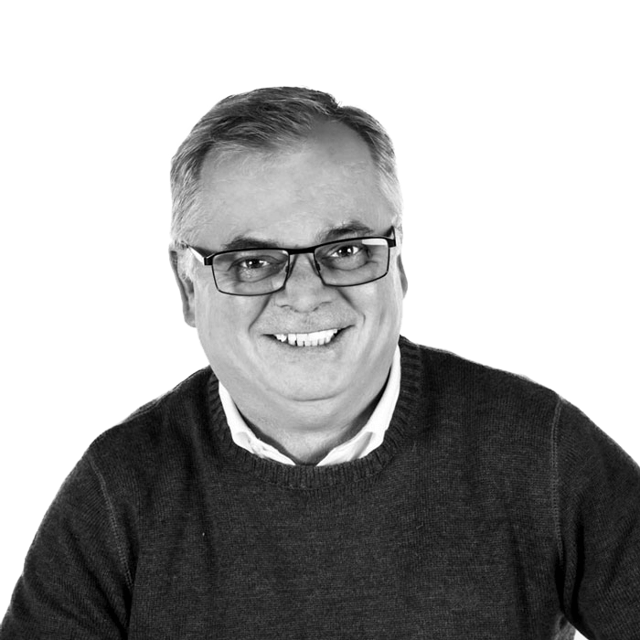 A man wearing glasses and a sweater is smiling in a black and white photo.
