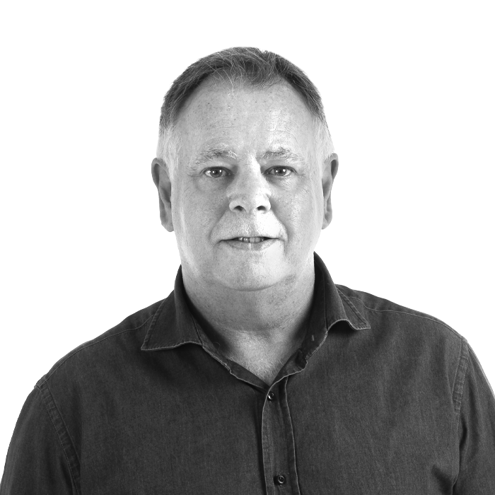 A man in a suit and white shirt is standing in front of a white background.