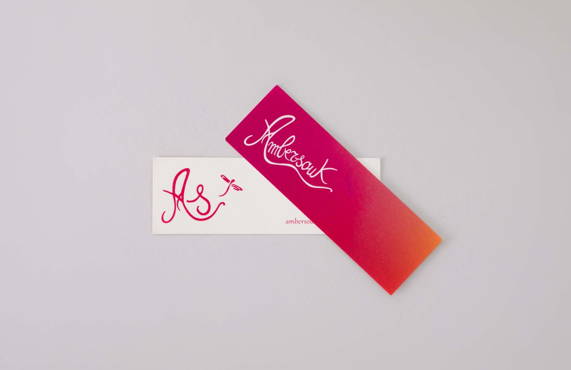 Two business cards with cursive writing. One is white, the other is pink and orange gradient. Both have pink text.