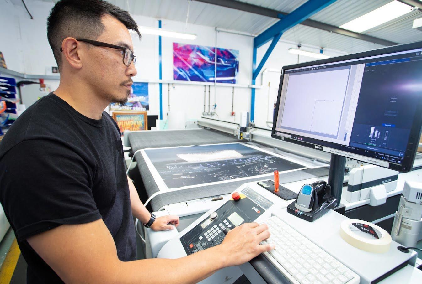 Man operating a large printing machine in a factory, focused on the computer screen.