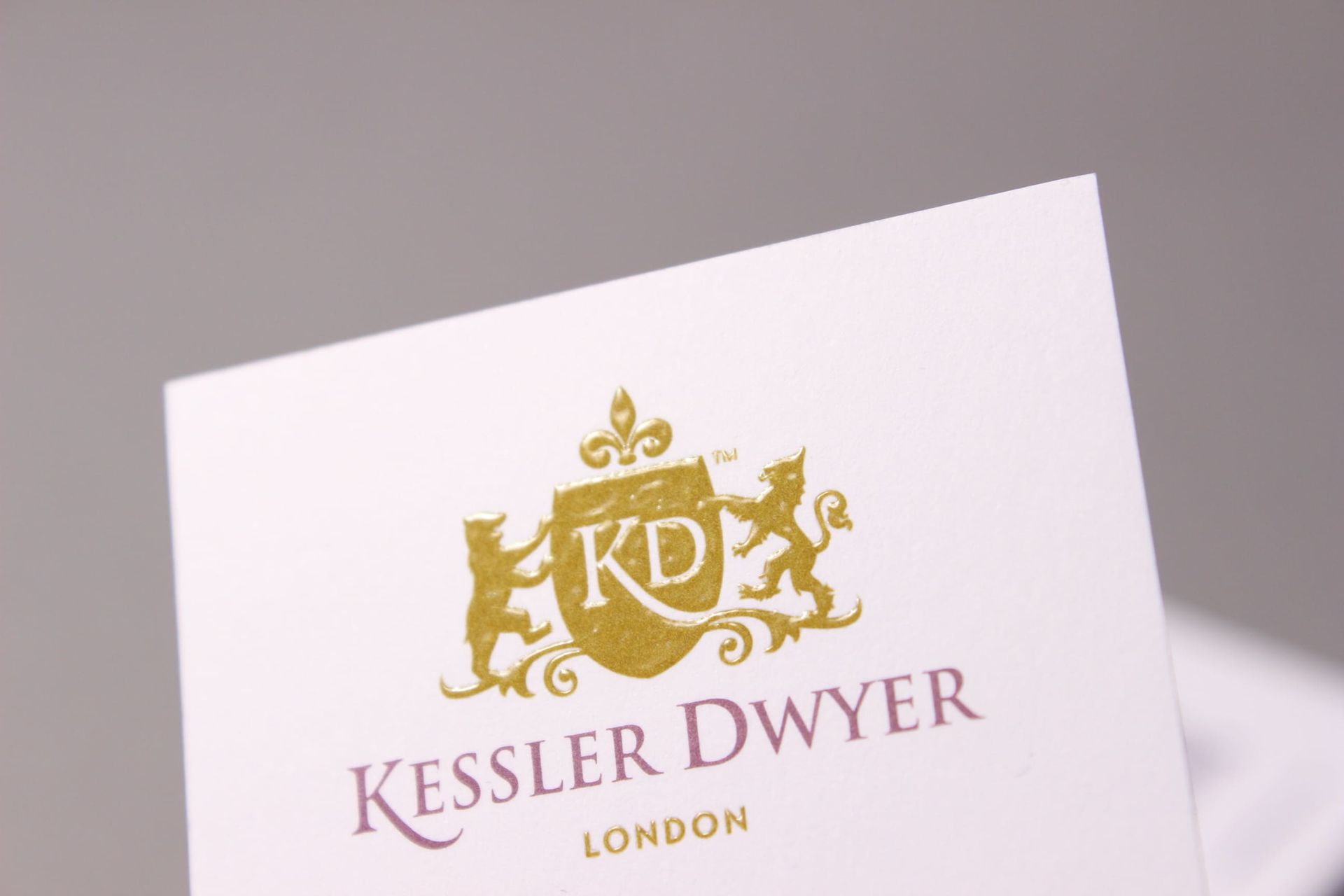 Gold logo for Kessler Dwyer London on a white card. A crest with