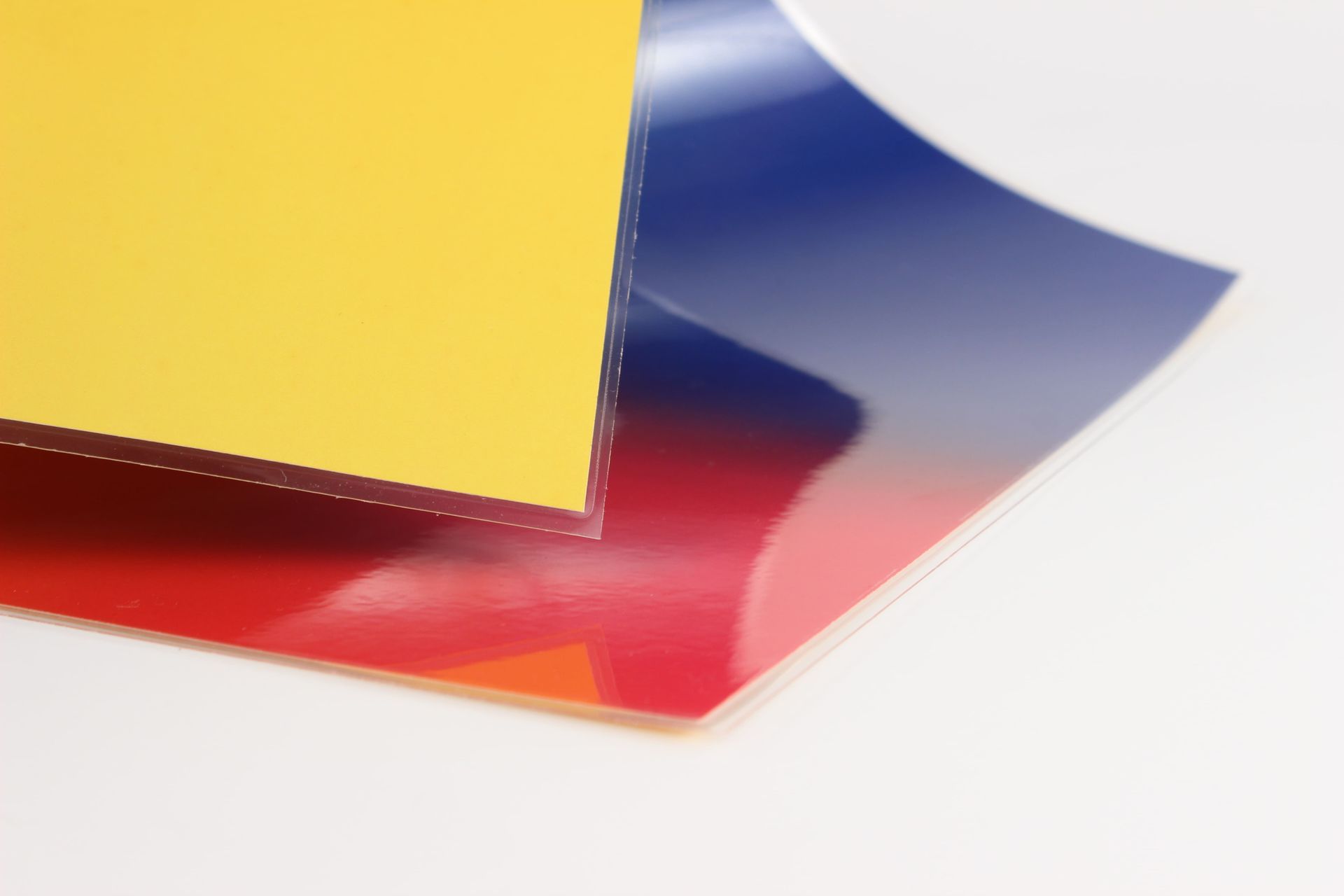 Sheets of yellow, red, and blue glossy paper, layered on a white surface.