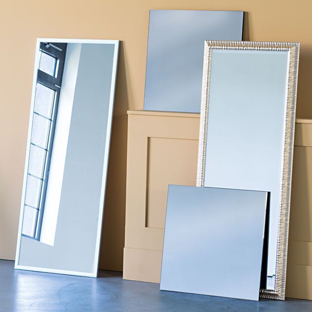 Five different sized mirrors leaning against a wall, reflecting a room.