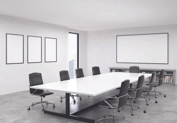 Modern conference room with a long white table, black chairs, and blank frames on white walls.