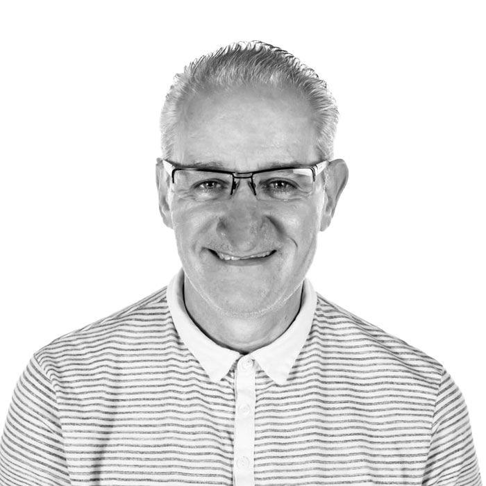 A man wearing glasses and a striped shirt is smiling in a black and white photo.