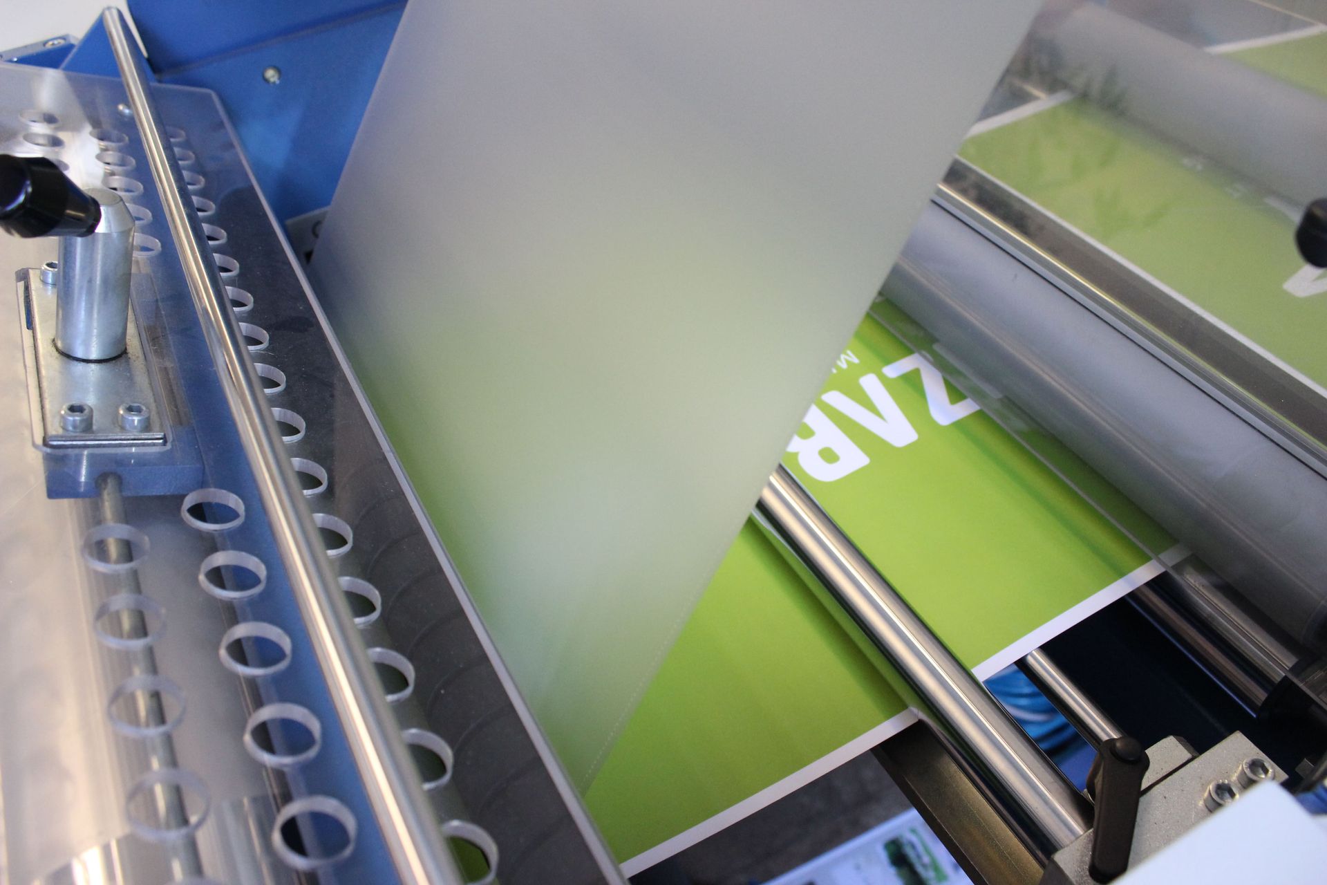 A machine applying a frosted film to a printed banner with white text on a green background.