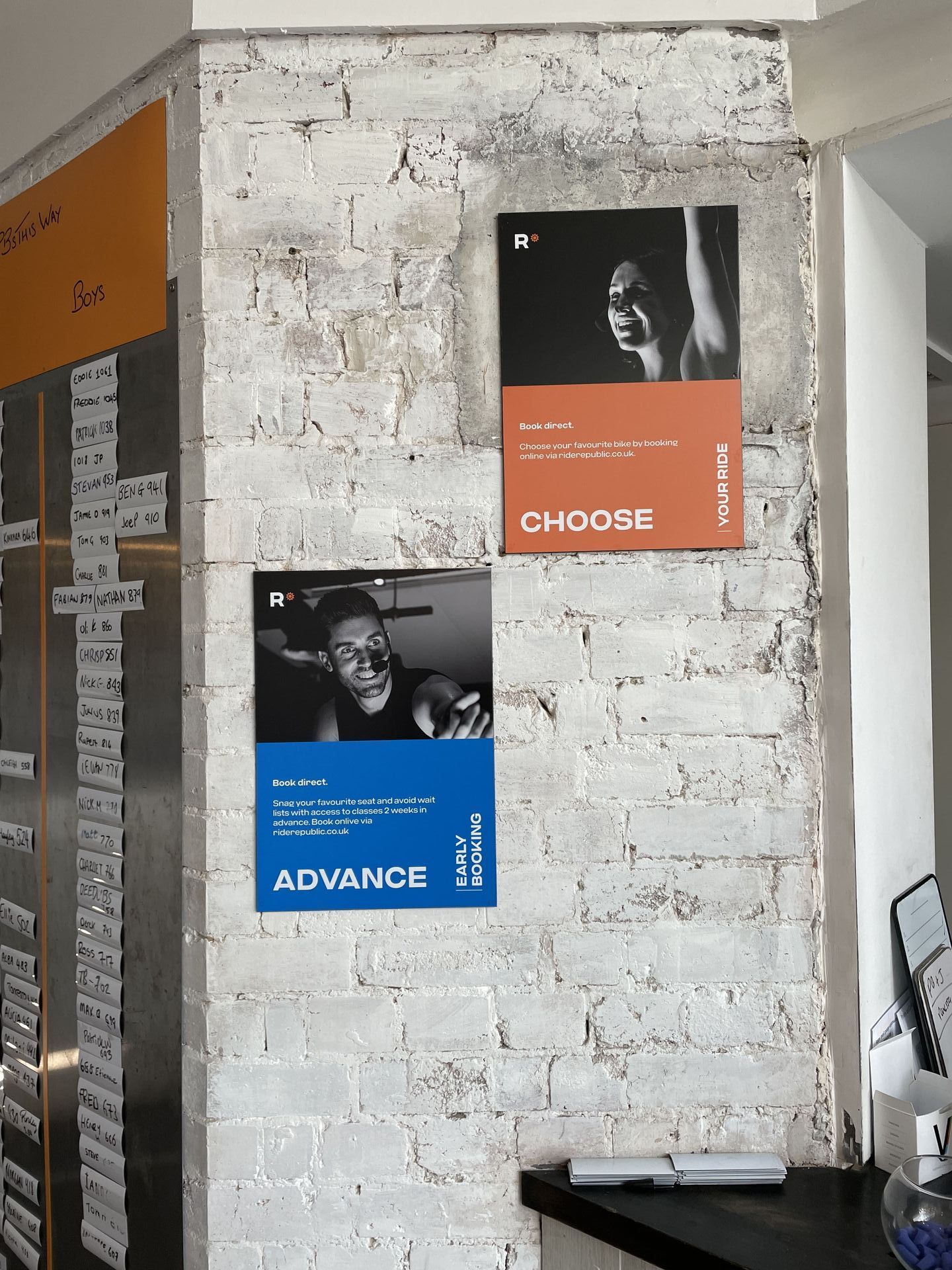 Two posters on a white brick wall. One with a blue background says