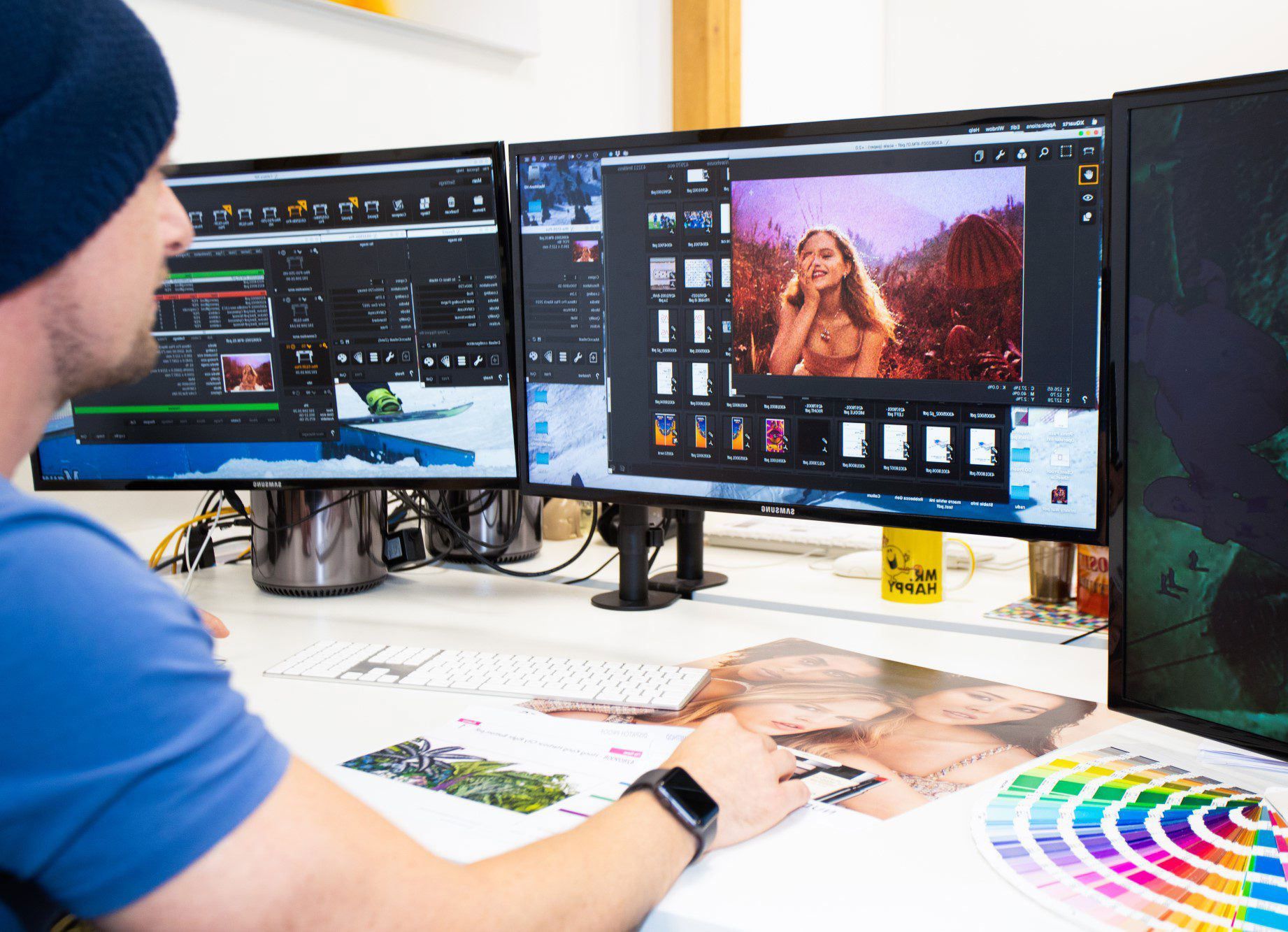 Man editing photos on multiple computer monitors, holding printouts, color wheel.