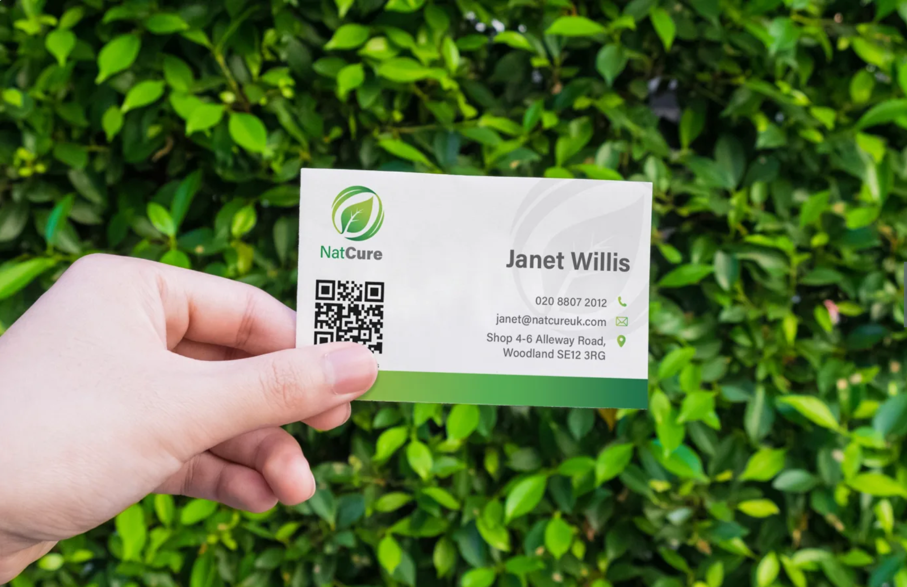 Person holding a business card for Plant Care in front of green foliage.