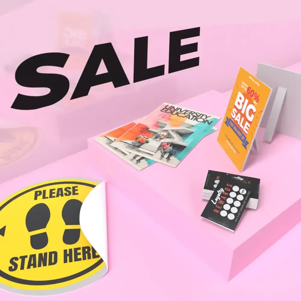 Sale promotion with various printed materials on a pink background, including flyers, signs, and floor decals.