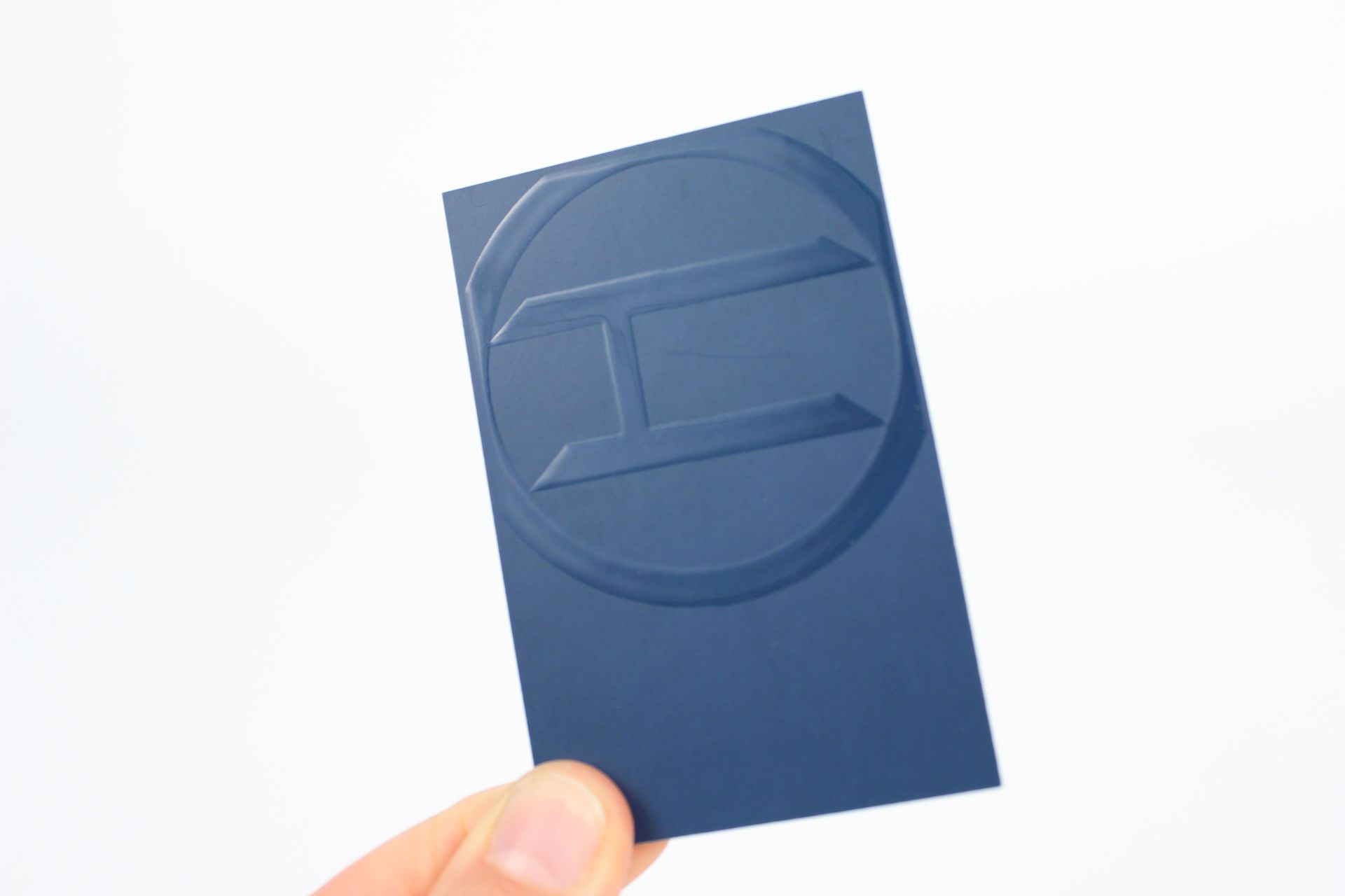 Hand holding a navy blue business card with an embossed letter