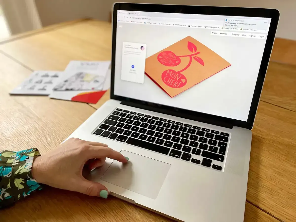 Person using a laptop displaying a cherry design, next to printed design examples.