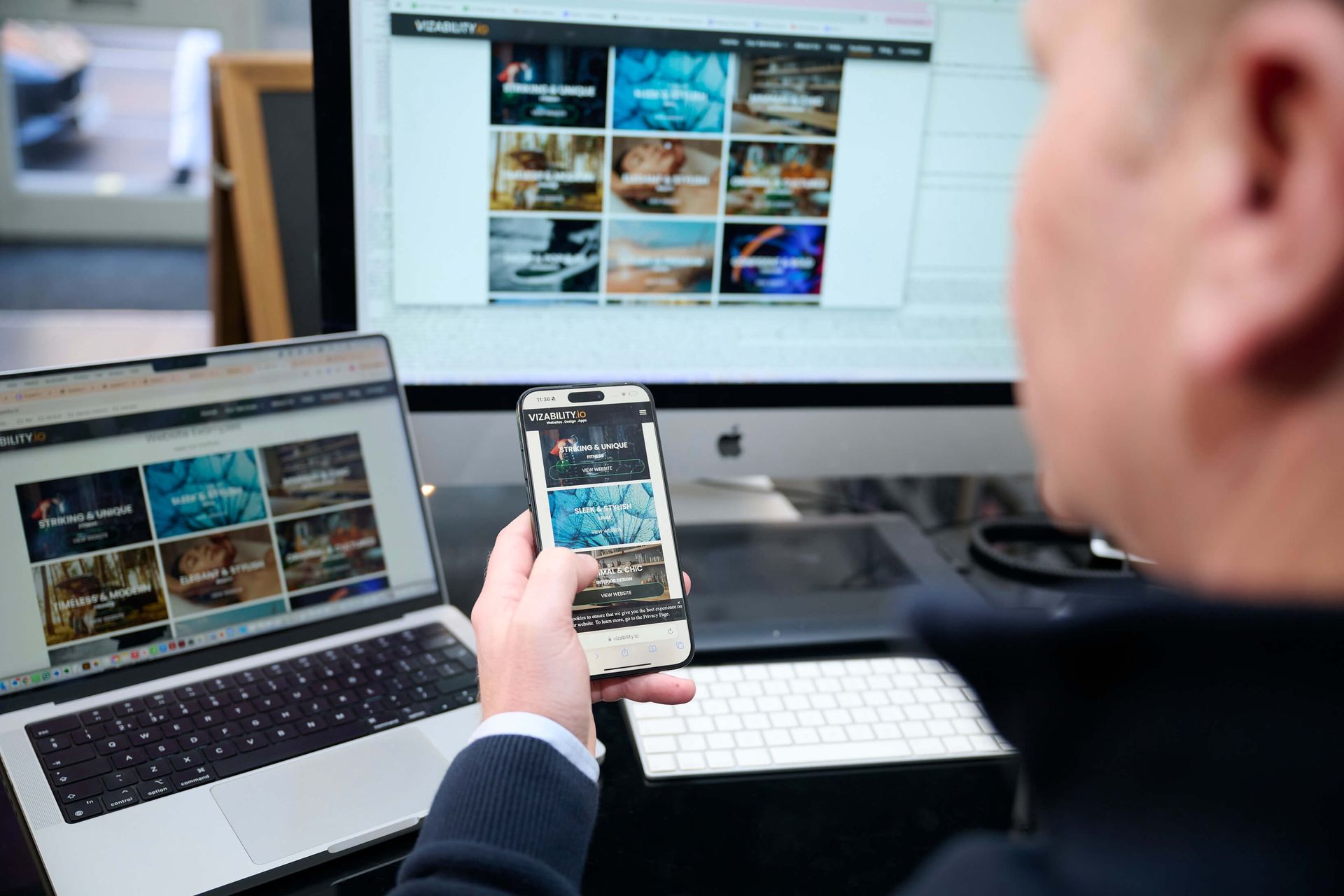 Man viewing a webpage on a laptop, monitor, and smartphone, possibly comparing content.
