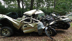 A wrecked car is sitting on the ground in the woods.